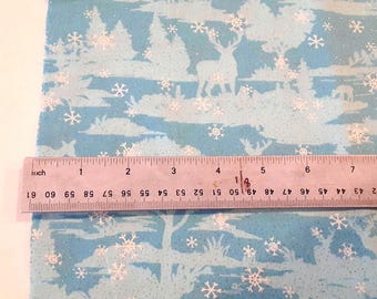 May include: A light blue fabric featuring a white winter forest pattern with deer and snowflakes, overlaid with a clear plastic ruler showing a width measurement of approximately 7.5 inches across the printed surface of the material.