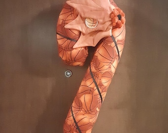 May include: A brown and orange candy cane shaped pillow with a basketball pattern. The top of the pillow has a brown felt leaf with a basketball design in the center.