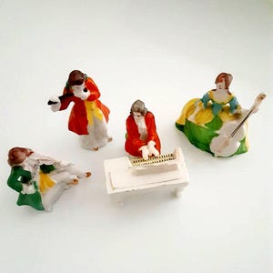 May include: A collection of miniature porcelain figurines depicting musicians. The figures are dressed in period clothing, with vibrant colors including red, green, yellow, and white. One figure plays a flute, another a piano, and a third a cello.