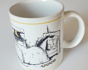 May include: A white ceramic mug featuring a black line drawing of a horse sleeping in a bed under a yellow crescent moon. The illustration includes the text UUUU in yellow near the bottom, framed by thin yellow horizontal lines at the top and base.