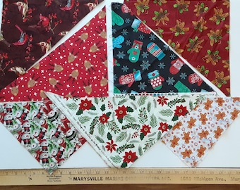May include: Six triangular fabric bandanas featuring various holiday prints including cardinals on dark brown, reindeer on red, mittens on black, pinecones on red, snowmen on white, and gingerbread men on white, displayed with a 28-inch ruler.