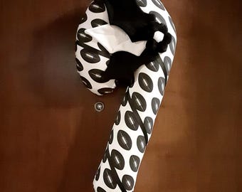 May include: A candy cane shaped fabric door hanger featuring a repeating pattern of black and white American footballs. The top section is adorned with a black fabric bat with white accents and a small black and white flower-shaped embellishment.