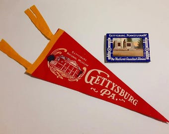 May include: A red felt pennant with the text "Gettysburg PA" and a graphic of a building. A small blue box with a picture of a monument and the text "Gettysburg, Pennsylvania" is also present.