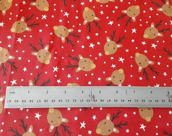 May include: A red fabric featuring a repeating pattern of brown reindeer heads with dark antlers and small white stars. A metal ruler is positioned across the bottom, showing a measurement scale of approximately 8.5 inches in length.
