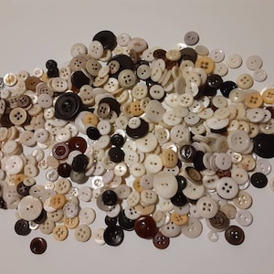 May include: A large collection of assorted buttons in various shades of white, brown, and black. The buttons are mostly round and have two or four holes.