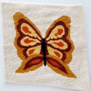 May include: A beige fabric wall hanging with a brown, orange, and yellow embroidered butterfly.