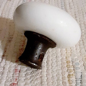May include: White porcelain door knob with a metal base. The knob is round and has a smooth surface. The base is brown and has a hole in the center.