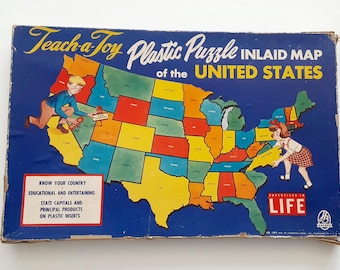 May include: Vintage "Teach-a-Toy Plastic Puzzle" of the United States. The box features a colorful map of the U.S. with children placing puzzle pieces. Text includes "Know Your Country" and "State Capitals". The box is blue with yellow, red, green, and orange states.
