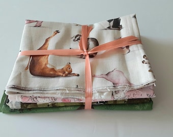 May include: A stack of folded fabric pieces tied with a peach-colored ribbon. The top layer is off-white with a repeating pattern of brown goats and pigs in various poses. The bottom layers feature pink and green patterns with animal motifs.