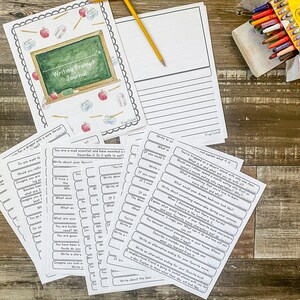 May include: A Writing Prompt Journal with a chalkboard design, pencils, and apples. Includes writing prompt cards and a lined paper sheet. A box of crayons is visible in the background. Educational supplies.