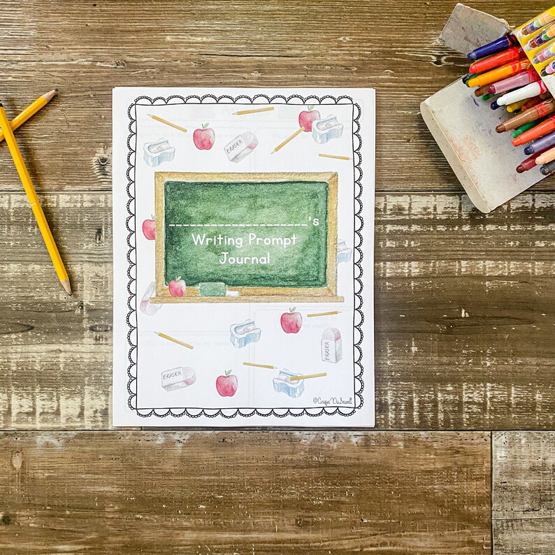 May include: A journal with a white cover and a black scalloped border. The cover features a green chalkboard design with the text "Writing Prompt Journal." It is decorated with watercolour illustrations of apples, pencils, erasers, and pencil sharpeners. Two pencils are on the left.