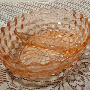 Puede incluir: Una fuente ovalada dividida, de color melocotón suave. La fuente presenta un patrón geométrico de diamantes en el borde exterior y un diseño en forma de abanico en el centro. La fuente es de vidrio y probablemente vintage.