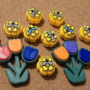 May include: A set of 10 colorful bee-themed resin molds. The molds are shaped like flowers and bees. The molds are yellow, orange, blue, purple, and green.