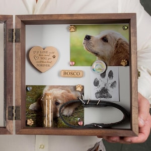 Könnte beinhalten: Eine hölzerne Schattenbox mit Scharniertür, die als Andenken für einen Hund dient. Die Box enthält Fotos, einen Pfotenabdruck, eine herzförmige Holzplakette und ein Halsband. Der Name des Hundes, Bosco, ist ebenfalls zu sehen.