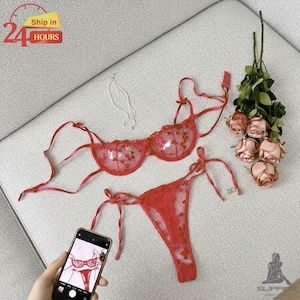 Op de afbeelding: Rode lingerie set met bloemenborduurwerk, bestaande uit een bh en string. De set wordt gepresenteerd met een smartphone met een foto van de lingerie, een zilveren ketting en een boeket roze rozen. De tekst "Ship in 24 HOURS" is zichtbaar.