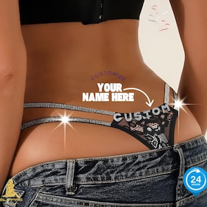 May include: Black lace thong with rhinestone straps and the word "CUSTOM" spelled out in rhinestones. The text "CUSTOMIZE YOUR NAME HERE" is also visible. The model is wearing blue jeans.