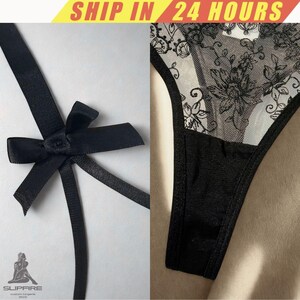 May include: Black lingerie set featuring a thong with floral lace detailing and a matching black bow. The thong has a sheer panel with a floral design. The bow is made of a satin-like material.