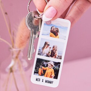Close-up of a Personalised Photo Strip Keyring featuring three custom photo slots and the names 'MIA & MUMMY'; a Custom Photo Gift Keyring and Personalized Photo Memory Keychain attached to a silver keyring, held against a soft pink background.