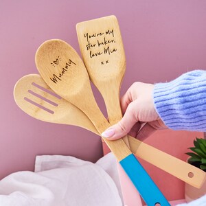 May include: Three wooden spoons with blue, beige, and natural wood handles. The spoons are engraved with the text "Mommy", "You're my star baker, love Mia, xx" and a heart symbol.
