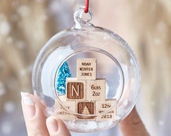 May include: A glass ornament with a miniature wooden block Christmas tree inside. The blocks are engraved with "Noah Winter Jones", "N", "6lbs 2oz", "1st Christmas", and "12th November 2018".