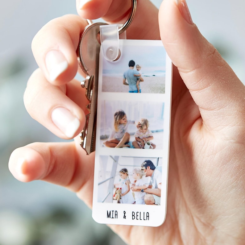 Hand holding a Personalised Photo Strip Keyring featuring three custom photo slots and the names 'MIA & BELLA'; a Custom Photo Gift Keyring and Personalized Photo Memory Keychain attached to a metal keyring.