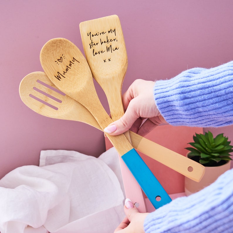 May include: Three wooden spoons with blue, beige, and natural wood handles. The spoons are engraved with the text "Mommy", "You're my star baker, love Mia, xx" and a heart symbol.