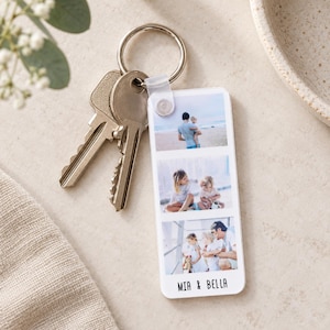 May include: A rectangular white acrylic keyring featuring three vertical photo slots displaying family moments, attached to a silver metal split ring with two keys. The bottom of the keyring is printed with the black text MIA & BELLA.