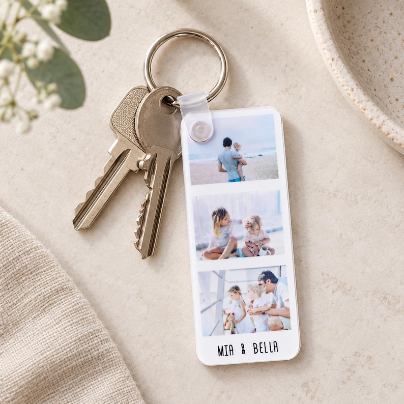 May include: A rectangular white acrylic keyring featuring three vertical photo slots displaying family moments, attached to a silver metal split ring with two keys. The bottom of the keyring is printed with the black text MIA & BELLA.
