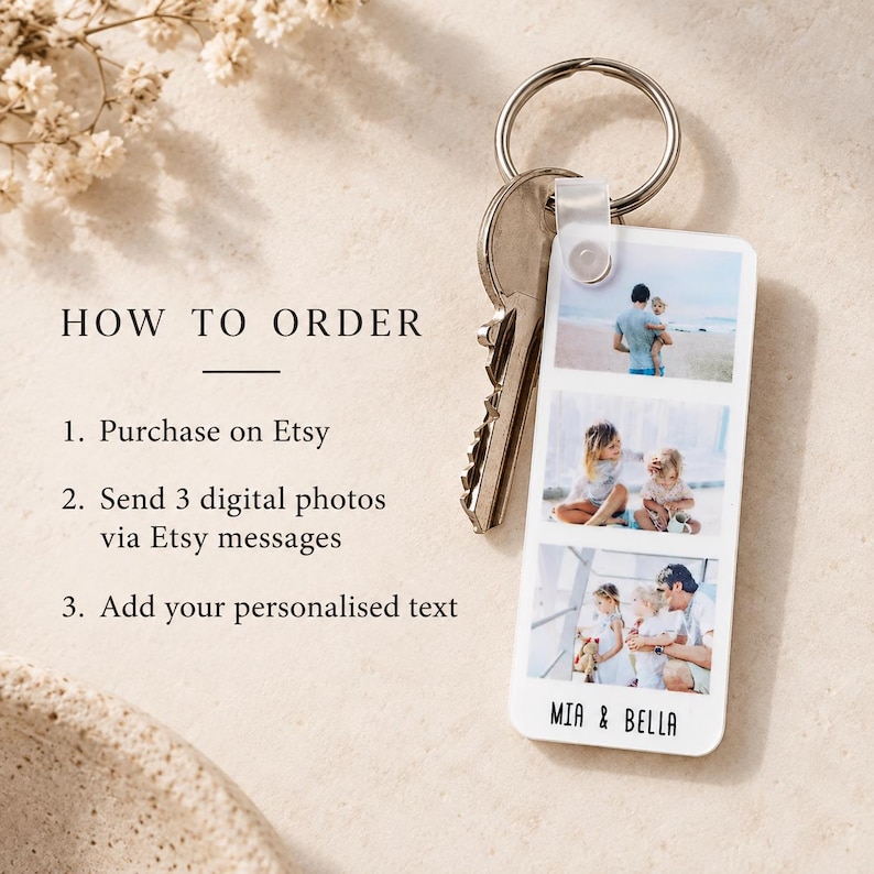 May include: A rectangular white keyring featuring three stacked colour photographs of people on a beach and in a park. The keyring includes a silver metal ring and key, with the text MIA & BELLA printed in black at the bottom of the white surface.