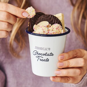 Pode incluir: Caneca de esmalte branco com borda azul e o texto "JESSICA'S Chocolate Treats" impresso no lado. A caneca está cheia de gotas de chocolate, pedaços de chocolate branco e granulado.