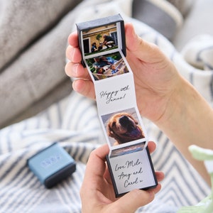 May include: A black box with a pull-out photo strip. The strip contains photos of a family and a dog. The box has a handwritten message that says "Happy 6th James!" and "Love Milo, Amy and Carol x".