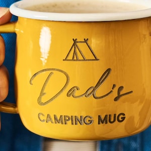 May include: Yellow camping mug with a white rim, featuring the text "Dad's CAMPING MUG" and a tent graphic. The mug is filled with a light-colored beverage.