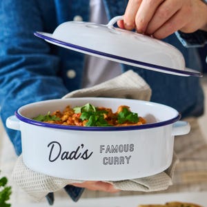 Könnte beinhalten: Weiße Emaille-Auflaufform mit blauem Rand und Deckel. Die Form trägt den Schriftzug "Dad's Famous Curry" auf der Vorderseite.