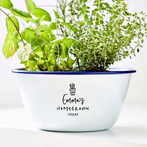 May include: White enamel planter with a blue rim, filled with green herbs. The planter has a black handwritten label that says "Emma's Homegrown Herbs" with a small drawing of a potted plant.