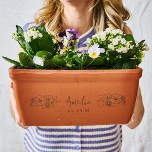 May include: A terracotta rectangular planter brimming with colourful flowers. The planter is personalised with the name "Amelia" and the date "22.09.86". Floral illustrations are on the sides.