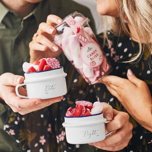 Pode incluir: Duas canecas de cerâmica branca com acabamento azul, cheias de doces rosa e vermelhos. As canecas são rotuladas como "Date" e "Night".