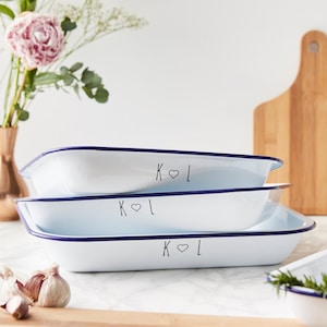 May include: Three white enamel baking dishes with blue rims stacked on top of each other. The dishes are personalized with the initials "K ♥ L" in black.