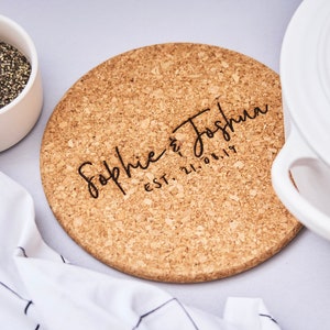 May include: Round cork trivet with the text "Sophie & Joshua EST. 21.08.19" in black lettering.
