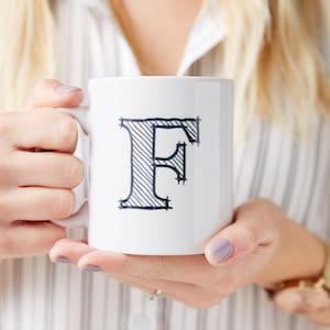 May include: White ceramic mug with a black outlined letter F. The letter is filled with black diagonal lines.