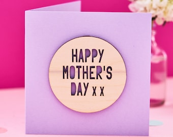 May include: A purple card with a wooden circle attached to the front. The circle has the words "Happy Mother's Day xx" cut out of it.
