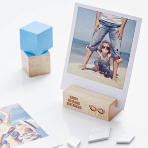 May include: A wooden photo holder with the text "Daddy Husband Superhero" and a mask graphic. The holder is displaying a photo of a father and child on a beach.