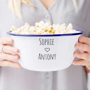 Puede incluir: Tazón de esmalte blanco con borde azul lleno de palomitas de maíz. El tazón tiene los nombres "Sophie" y "Antony" escritos con un símbolo de corazón entre los nombres.