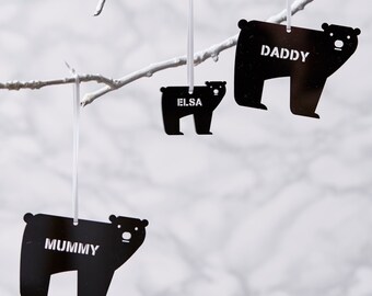 May include: Three black bear silhouette ornaments with the words "Mummy", "Daddy", and "Elsa" hanging from a white branch.