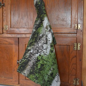 May include: A kitchen towel with a birch tree bark pattern in shades of green, white, and black hangs from a wooden cabinet. The towel's design mimics the texture and colors of birch bark, creating a natural aesthetic.