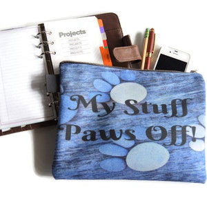 May include: A blue zippered pouch with a white background and a pattern of blue and white pebbles. The pouch has the text "My Stuff Paws Off!" printed in black.