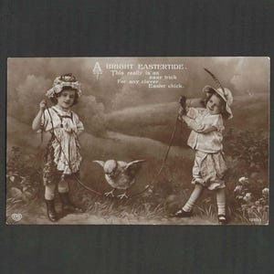 May include: A vintage sepia-toned postcard featuring two children holding a rope with a small chick standing in the centre. The text reads: A BRIGHT EASTERTIDE. This really is an easy trick For any clever Easter chick. The children wear period clothing.