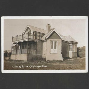 May include: A vintage black and white postcard featuring a two-story house with a balcony and a chimney. The house has a light-colored exterior and a gabled roof. Text on the postcard reads "Sunny holme - Bigbury-on-Sea."
