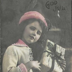 Carte postale de Noël antique God Jul RPPC - Fille avec des cadeaux dans un pull confortable et un chapeau 1914 avec drapeau