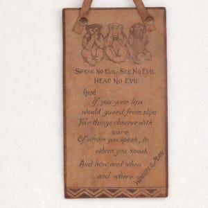 May include: A rectangular tan leather wall hanging featuring an embossed illustration of three monkeys and the text: Speak No Evil-See No Evil Hear No Evil. Below, a poem is inscribed, ending with the text Winnipeg, Man. It has a leather strap.