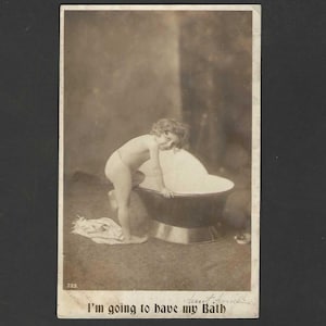 May include: Vintage sepia-toned photograph of a child preparing for a bath. The child is standing near a large, dark-colored bathtub. Text at the bottom reads, "I'm going to have my Bath."
